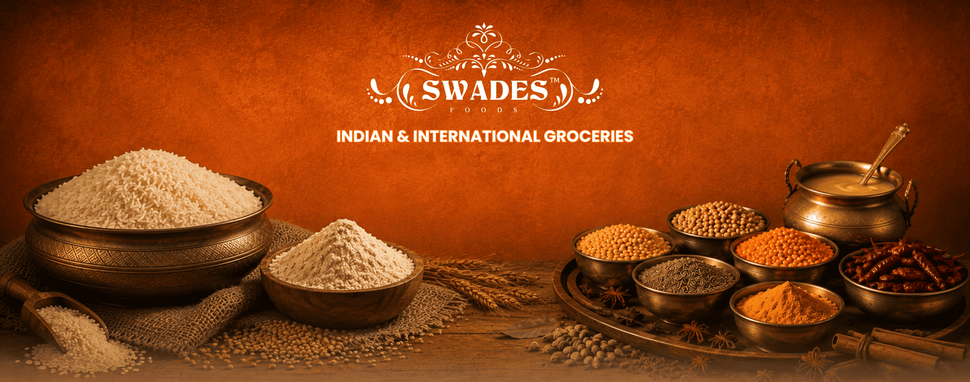 A warm, rustic promotional banner for Swades Indian & International Groceries, featuring various spices, grains, and lentils arranged in traditional brass and clay bowls on a wooden table against a textured orange-brown background.